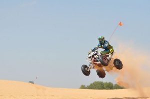 An ATV racer catches air as they fly over a desert landscape