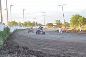 Three ATVs race around the bend with another close behind as an official waves a checkered flag