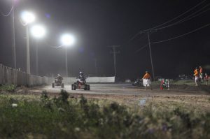 An ATV night race shows two racers going around the track and the official holding a white flag