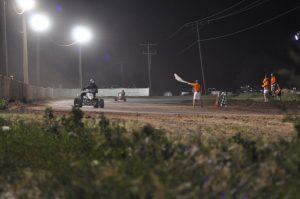 An ATV night race shows two racers close behind one another and the official holding a checkered flag