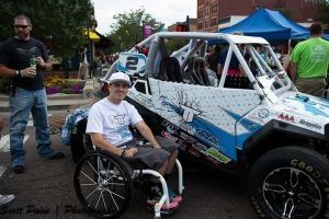 A young person in a wheelchair poses next to a white UTV