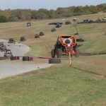 An orange UTV is following behind a line of other UTVs during a competition